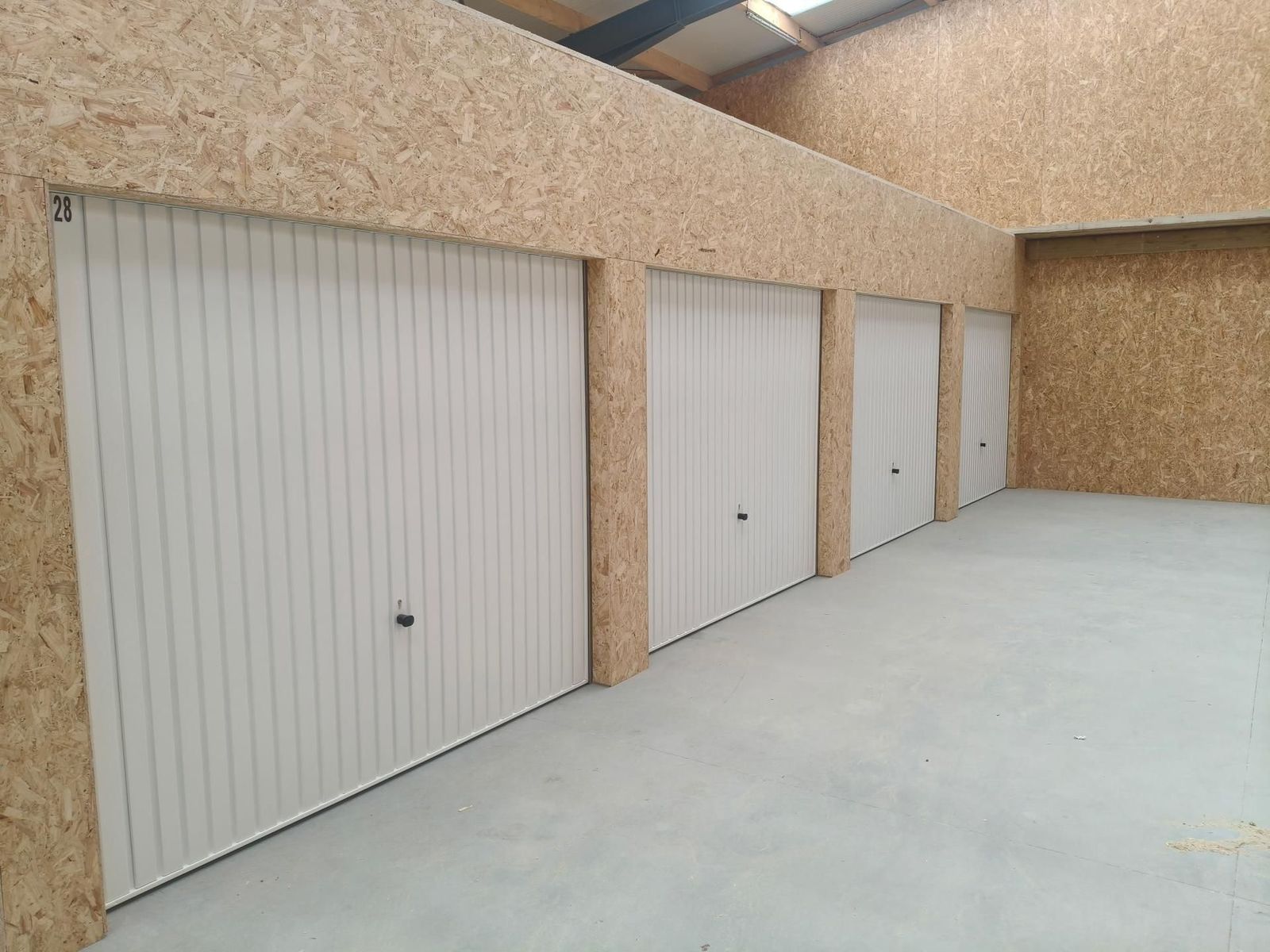 Rangée de box aux portes basculantes blanches, cloisons en bois, box n° 28 au premier plan
